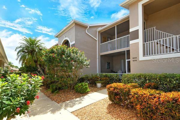 A two-story apartment building exterior features a screened balcony, white railings, and landscaped shrubbery — 9641 CASTLE POINT DRIVE UNIT 1215, SARASOTA, FL