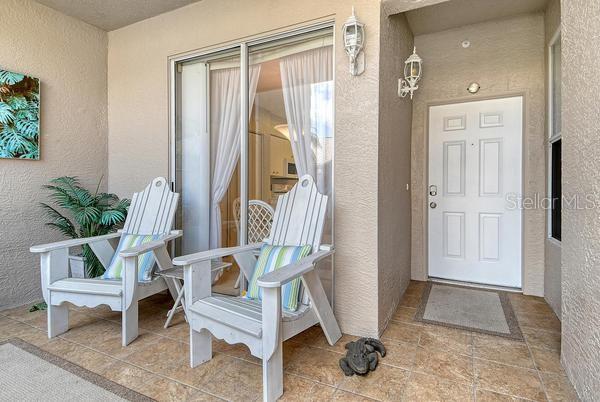 A covered patio features two white Adirondack chairs, a small side table, and a white door — 9641 CASTLE POINT DRIVE UNIT 1215, SARASOTA, FL