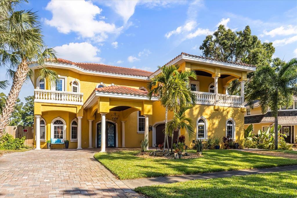 A two-story yellow stucco house features a tiled roof, arched windows, and a paved driveway — 911 JUNGLE AVENUE N, ST PETERSBURG, FL