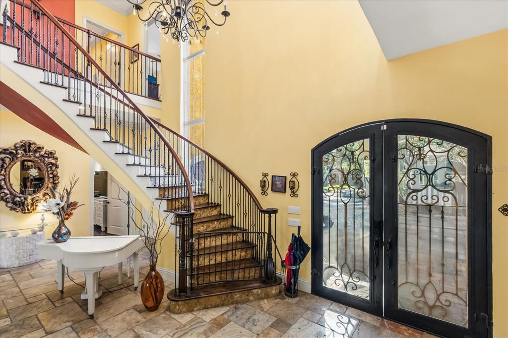An entryway features a curved staircase, a white piano, and double glass-paneled doors — 911 JUNGLE AVENUE N, ST PETERSBURG, FL