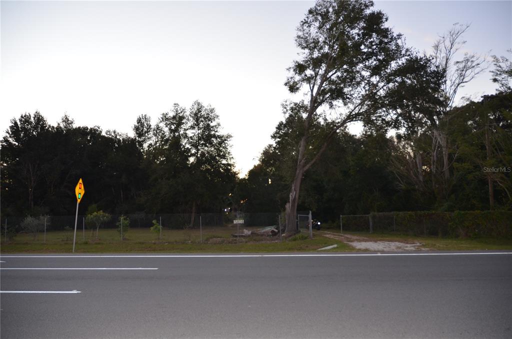 A fenced, grassy lot with trees sits beside a paved road with a traffic sign — 5024 PLYMOUTH SORRENTO ROAD, APOPKA, FL