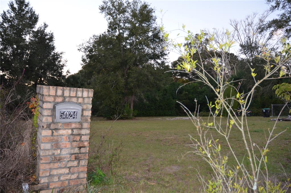 A brick mailbox stands in the foreground of a vacant, grassy residential lot — 5024 PLYMOUTH SORRENTO ROAD, APOPKA, FL