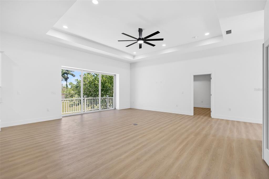 A spacious, empty room features light wood-look flooring, a tray ceiling with a fan, and sliding doors — 200 LEACH DRIVE, PUNTA GORDA, FL