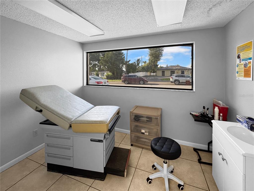 A medical examination room features a treatment table, a rolling stool, and a sink — 5438 TROUBLE CREEK ROAD, NEW PORT RICHEY, FL