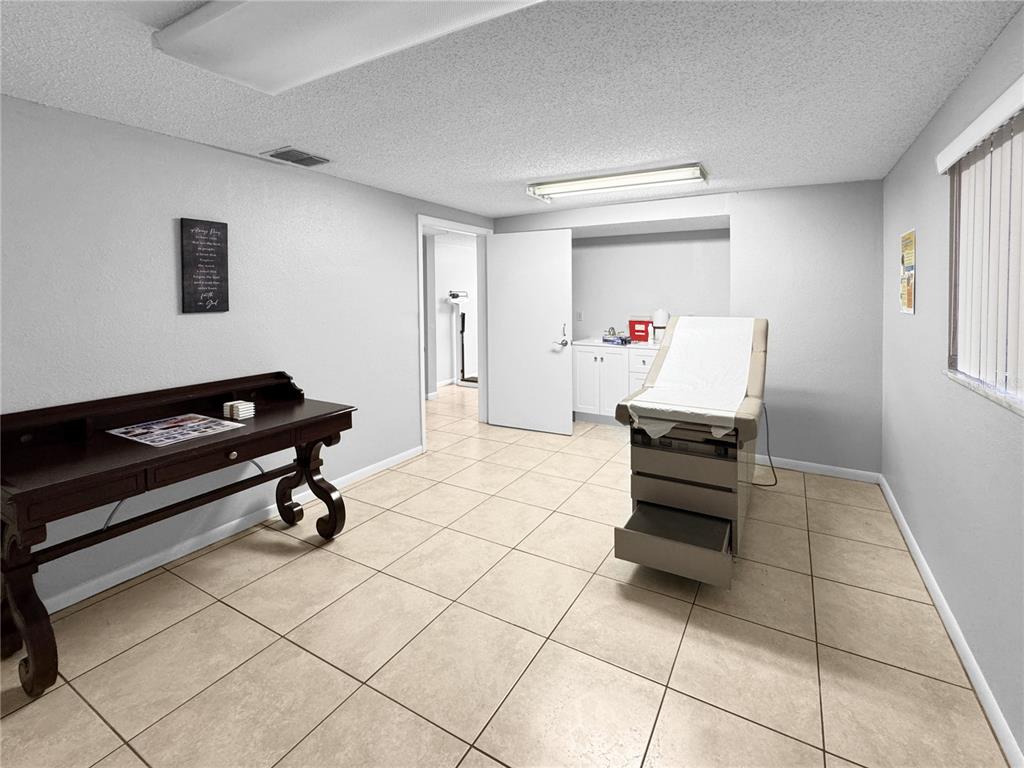 A medical examination room features a treatment table, a dark wood desk, and tile flooring — 5438 TROUBLE CREEK ROAD, NEW PORT RICHEY, FL