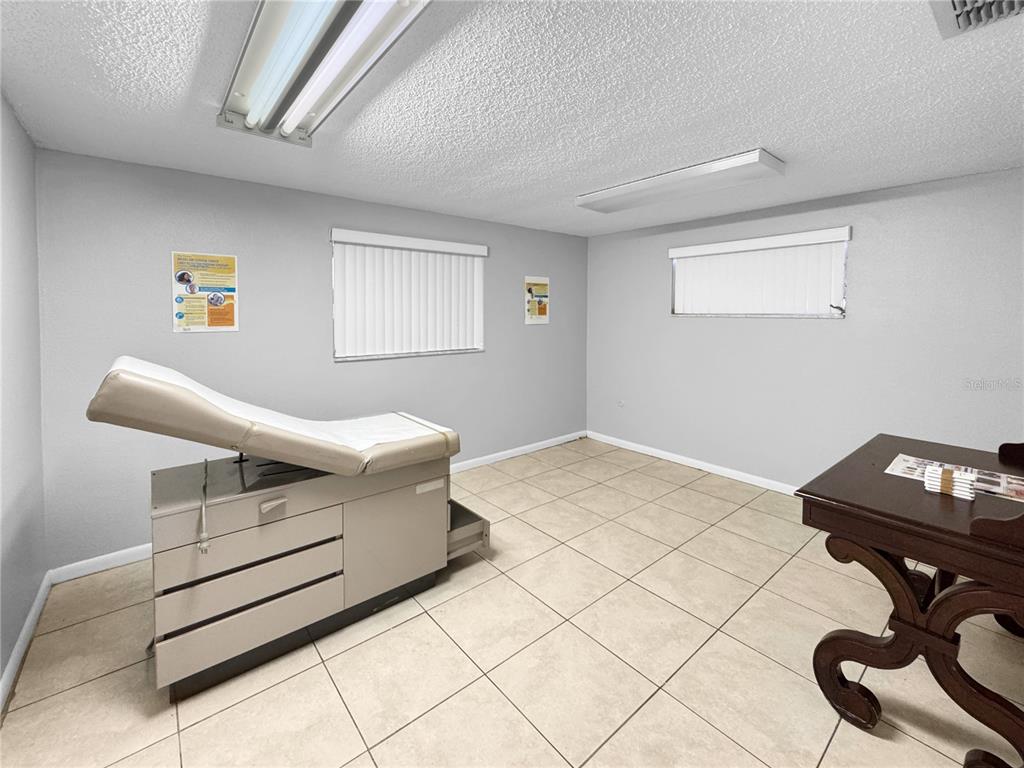 A medical examination room features a beige exam table, tile flooring, and a wooden desk — 5438 TROUBLE CREEK ROAD, NEW PORT RICHEY, FL
