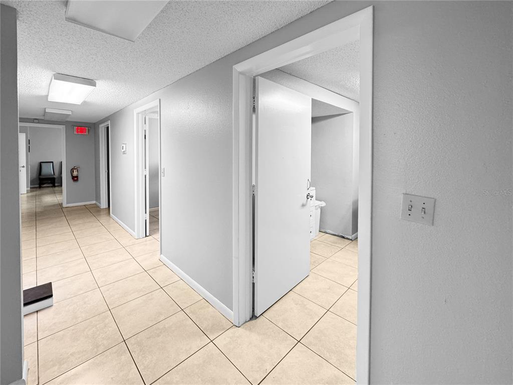 A hallway with light-colored tile flooring leads to multiple doorways and an exit sign — 5438 TROUBLE CREEK ROAD, NEW PORT RICHEY, FL