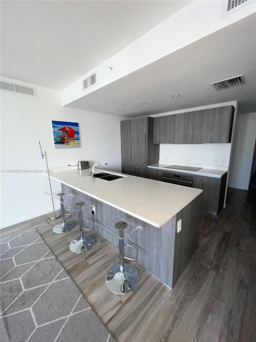 A modern kitchen features a white island, gray cabinetry, and three chrome bar stools — 801 S Miami Ave # 3304, Miami FL 33130, MIAMI, FL