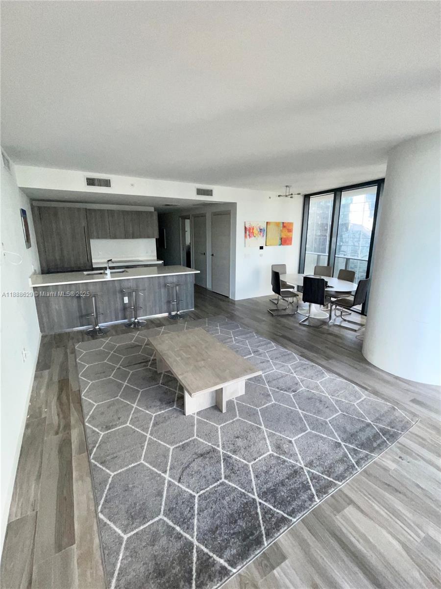 An open-concept living and dining area features a kitchen island, wood-look flooring, and floor-to-ceiling windows — 801 S Miami Ave # 3304, Miami FL 33130, MIAMI, FL