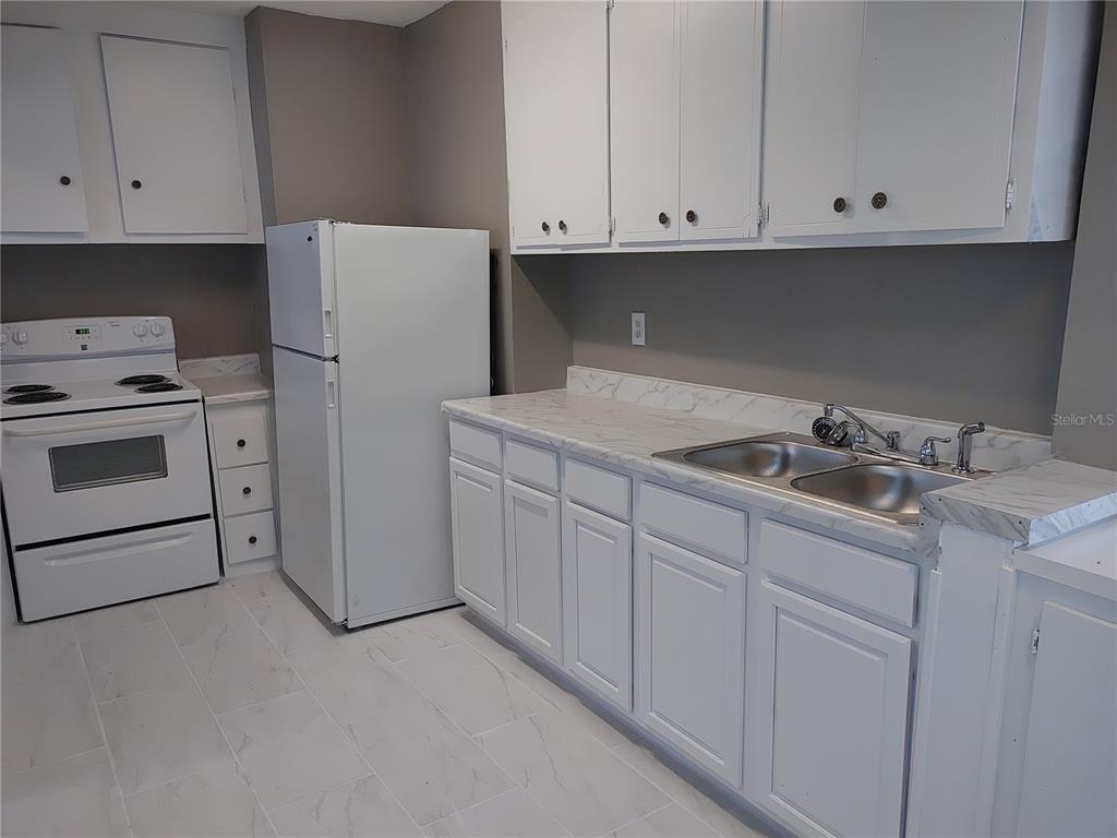 A kitchen features white cabinets, a white stove, a refrigerator, and marble-patterned countertops — 1090 SAINT CLAIR STREET, JACKSONVILLE, FL