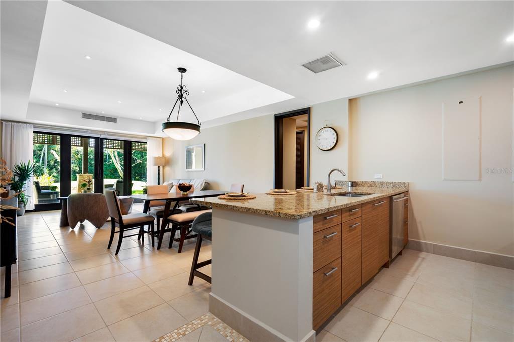 A kitchen with granite countertops and wood cabinets opens to a dining area and patio — 7000 BAHIA BEACH BLV LAS VERANDAS UNIT 3118, RIO GRANDE, PR