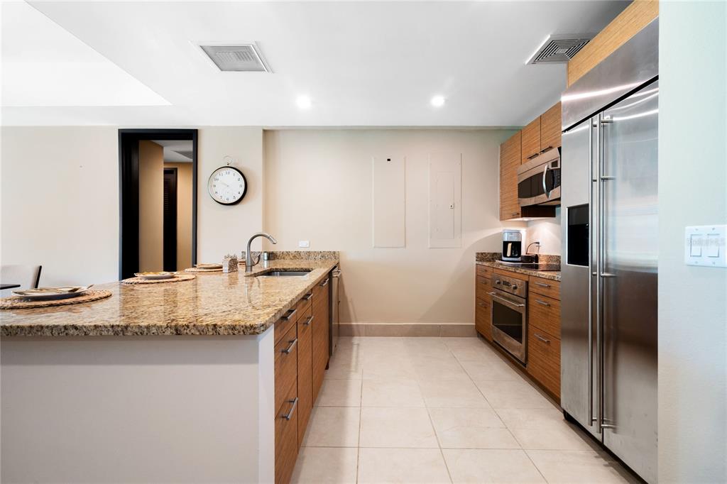 A modern kitchen features granite countertops, wood cabinetry, and stainless steel appliances — 7000 BAHIA BEACH BLV LAS VERANDAS UNIT 3118, RIO GRANDE, PR