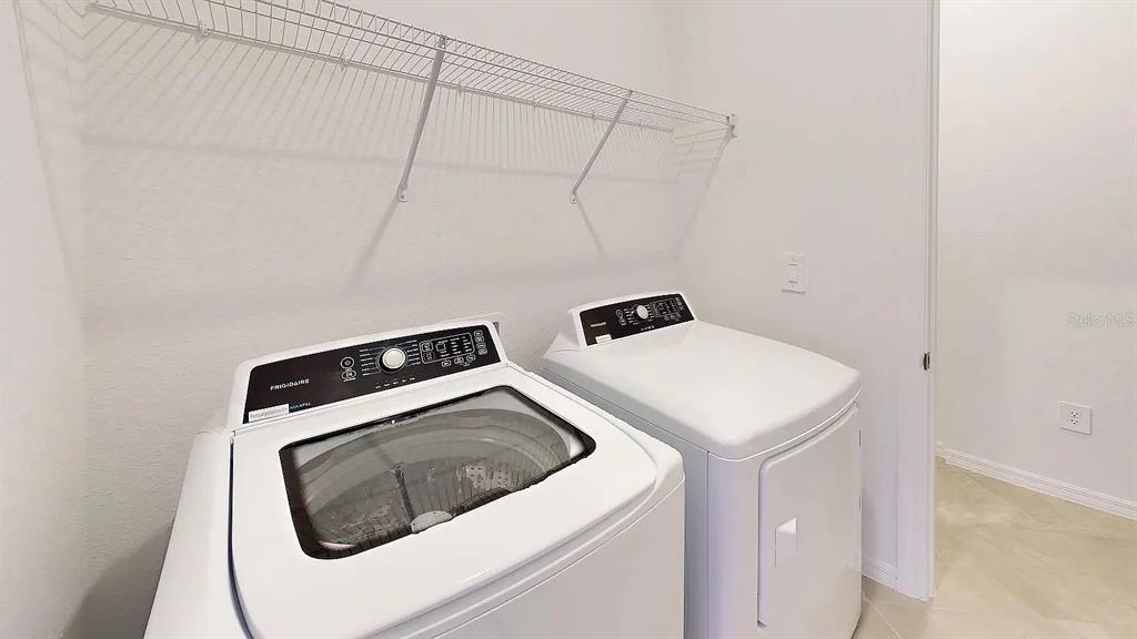 A laundry room features a white top-load washer and dryer beneath a wire wall shelf — 2017 GARDENIA AVENUE, PORT CHARLOTTE, FL