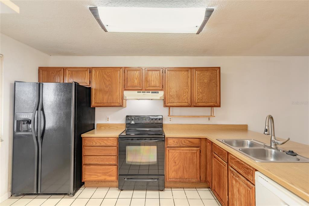 A kitchen features wood cabinets, black appliances, a double sink, and white tile flooring — 3548 FOREST BRANCH DRIVE UNIT C, PORT ORANGE, FL