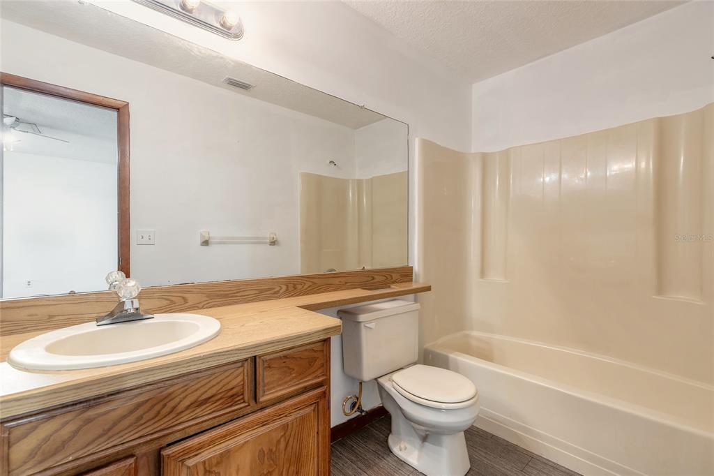 A bathroom features a wood vanity, a large mirror, a toilet, and a beige tub surround — 3548 FOREST BRANCH DRIVE UNIT C, PORT ORANGE, FL