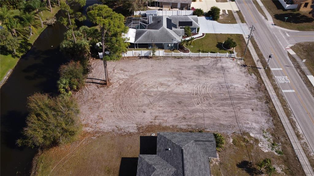 An aerial view shows a cleared, sandy vacant lot situated between a canal and a road — 23326 PEACHLAND BOULEVARD, PORT CHARLOTTE, FL