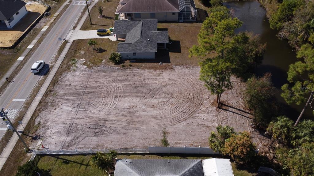 An aerial view shows a cleared, sandy residential lot situated between a road and canal — 23326 PEACHLAND BOULEVARD, PORT CHARLOTTE, FL