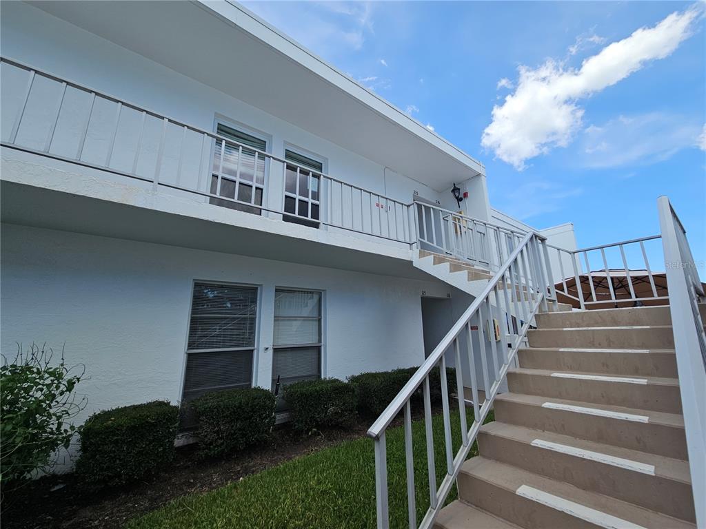 A two-story white apartment building features an exterior staircase and a second-floor balcony — 1655 S HIGHLAND AVENUE UNIT B215, CLEARWATER, FL