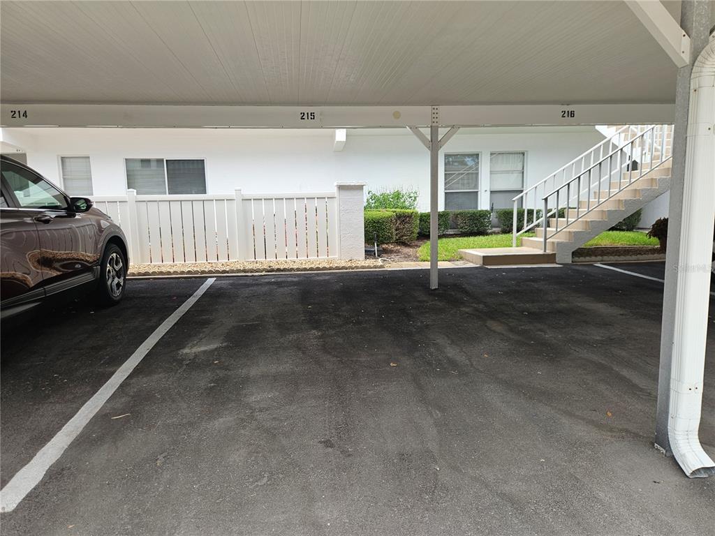 A covered parking area features numbered spaces and a staircase leading to an apartment building — 1655 S HIGHLAND AVENUE UNIT B215, CLEARWATER, FL