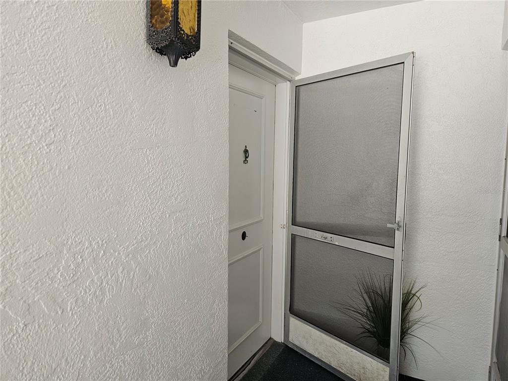 A white door with a screen door stands in a textured white entryway — 1655 S HIGHLAND AVENUE UNIT B215, CLEARWATER, FL