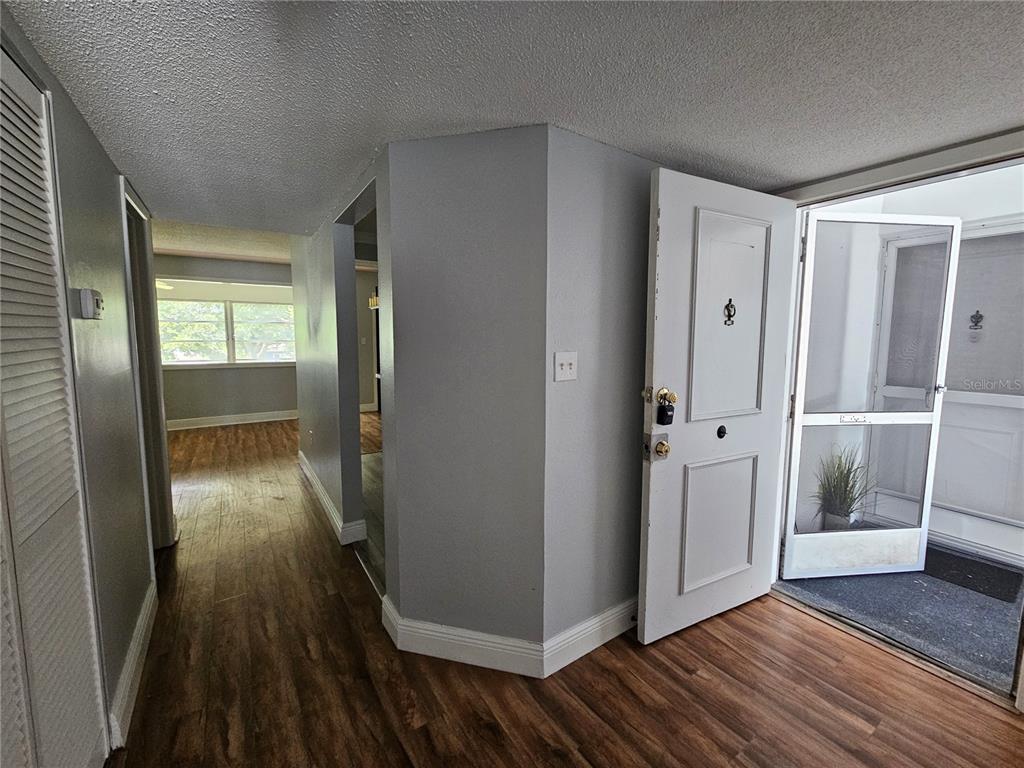 An entryway with wood-look flooring leads to an interior hallway and an open front door — 1655 S HIGHLAND AVENUE UNIT B215, CLEARWATER, FL