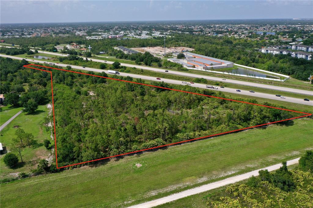 An aerial view shows a triangular, tree-covered plot of land adjacent to a highway — 24869 NOVA LANE, PORT CHARLOTTE, FL