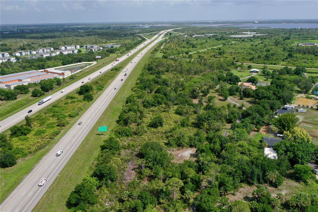 An aerial view shows a multi-lane highway running through a wooded area with nearby buildings — 24869 NOVA LANE, PORT CHARLOTTE, FL