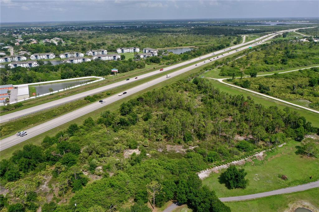 An aerial view shows a highway running past a wooded lot and residential apartment buildings — 24869 NOVA LANE, PORT CHARLOTTE, FL