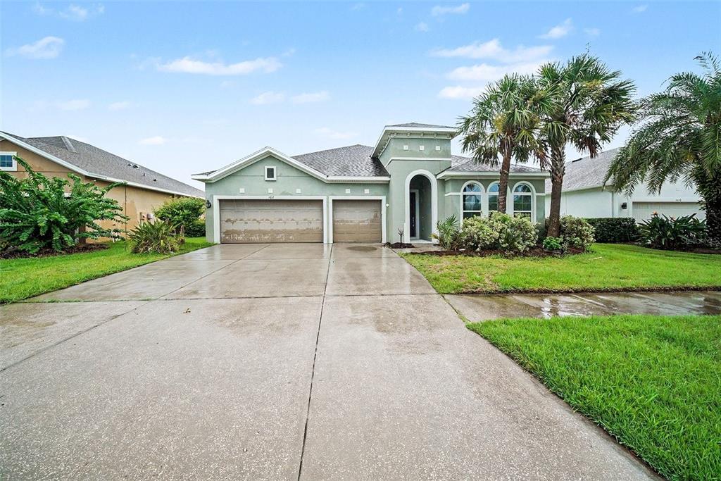 A light green single-story house with a three-car garage and a paved driveway — 1832 TONKA TERRACE, WESLEY CHAPEL, FL