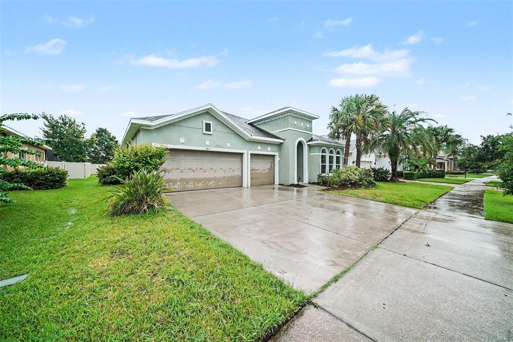 A light green single-story house with a three-car garage and a concrete driveway — 1832 TONKA TERRACE, WESLEY CHAPEL, FL