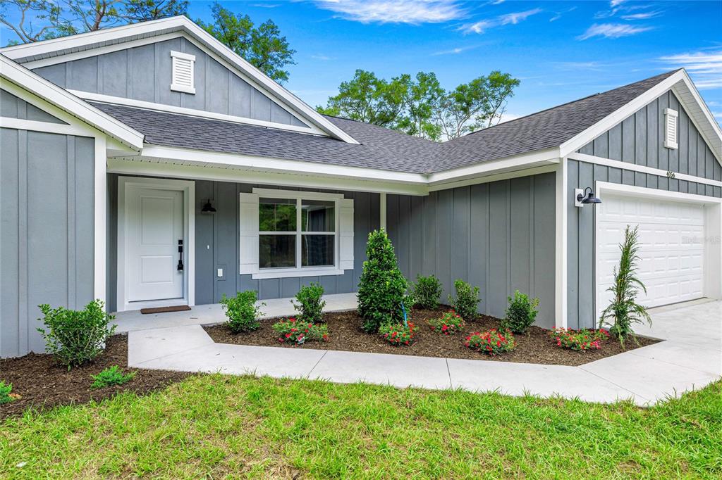 A gray, single-story house features a white front door, a garage, and a landscaped yard — 4056 SW 156TH COURT, OCALA, FL