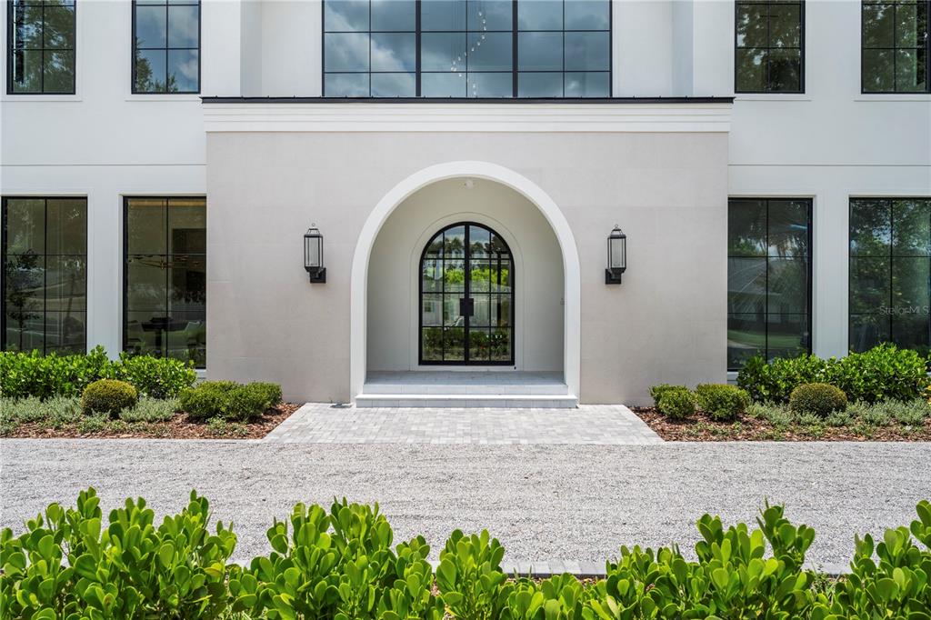 The exterior of a white house features a central arched entryway with black-framed glass doors — 1525 GRANVILLE DRIVE, WINTER PARK, FL