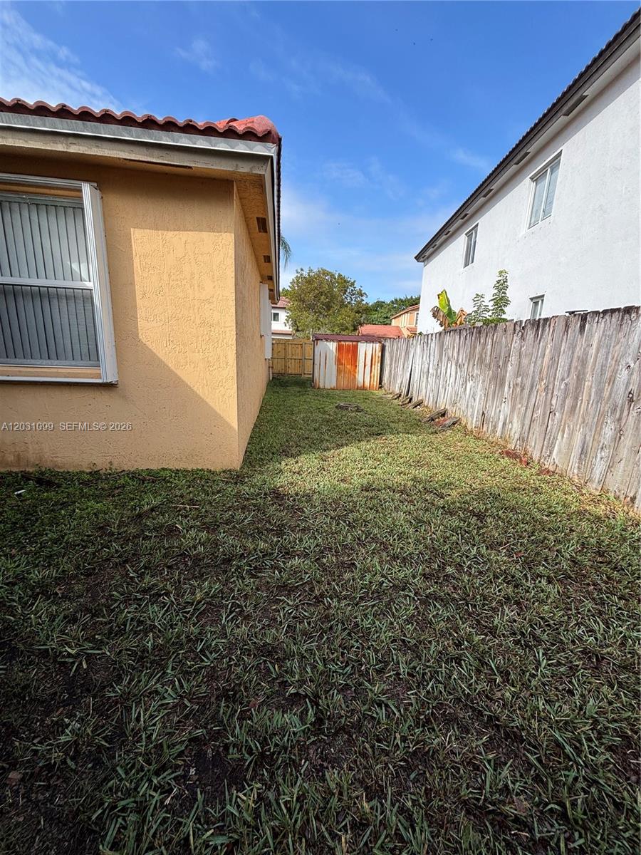A narrow grassy side yard sits between a tan house and a wooden fence — 2103 NE 38th Rd, Homestead FL 33033, HOMESTEAD, FL