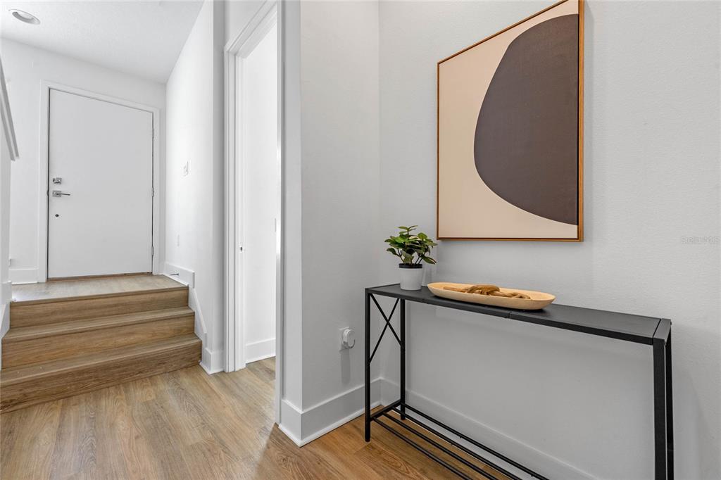 A modern entryway features wood-look stairs, a black console table, and abstract wall art — 52 W HARDING STREET UNIT A, ORLANDO, FL
