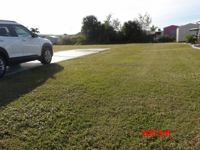 A white SUV is parked on a concrete pad next to an open grassy lot — 1538 BLUE HERON DRIVE, ENGLEWOOD, FL