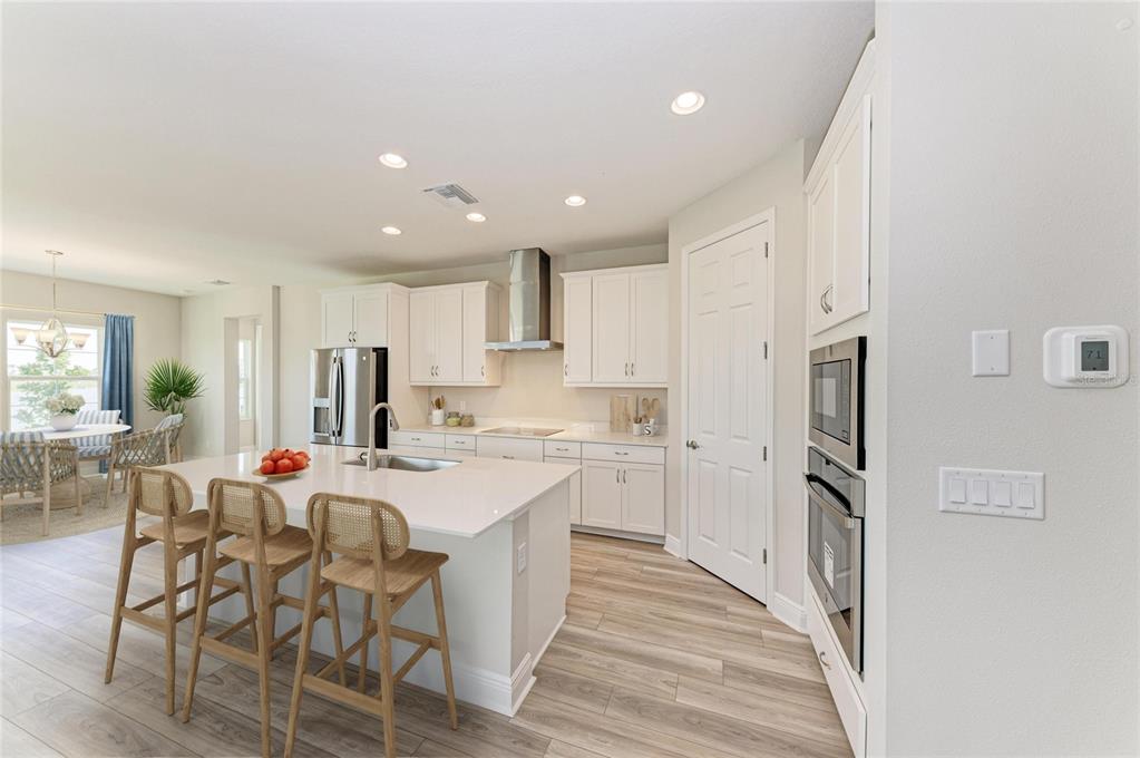 A modern kitchen features white cabinetry, a central island with bar stools, and stainless appliances — 10148 SURREY ROSE DRIVE, SAN ANTONIO, FL