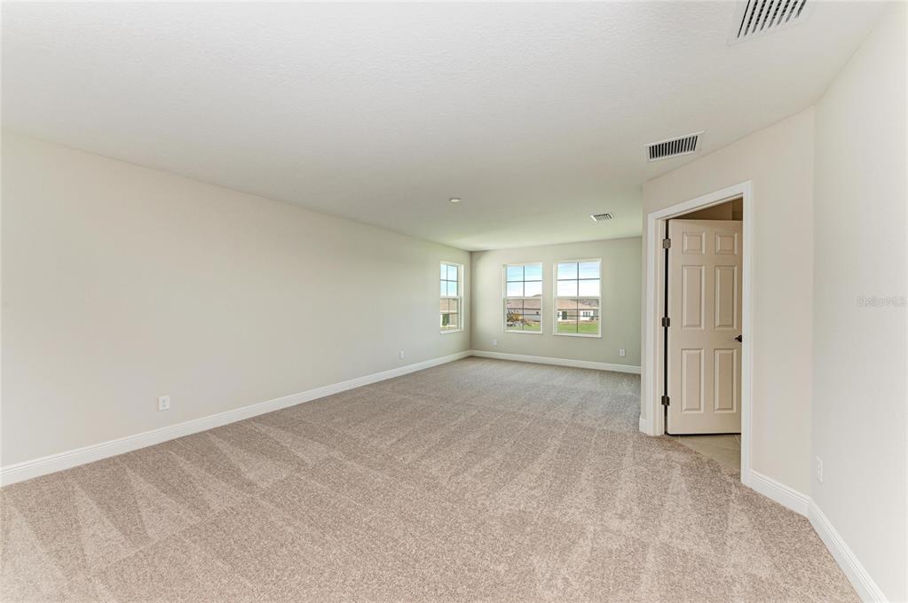 An empty room with beige carpet, light-colored walls, and windows overlooking a suburban neighborhood — 10148 SURREY ROSE DRIVE, SAN ANTONIO, FL