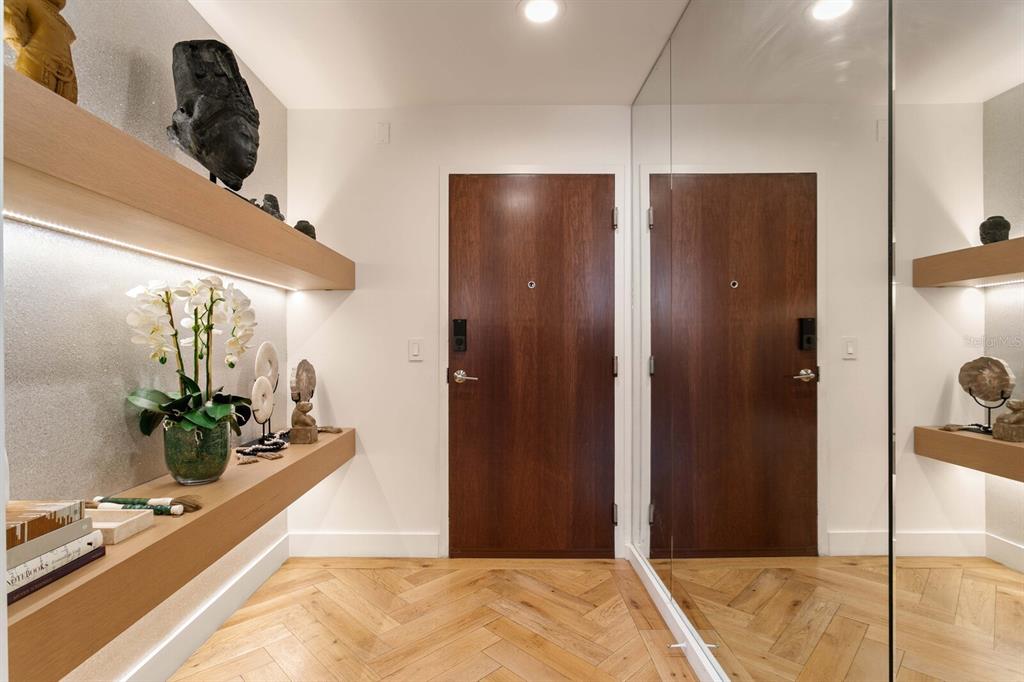 An entryway features herringbone wood floors, floating shelves with decor, and a mirrored wall — 777 N ASHLEY DRIVE UNIT 806, TAMPA, FL