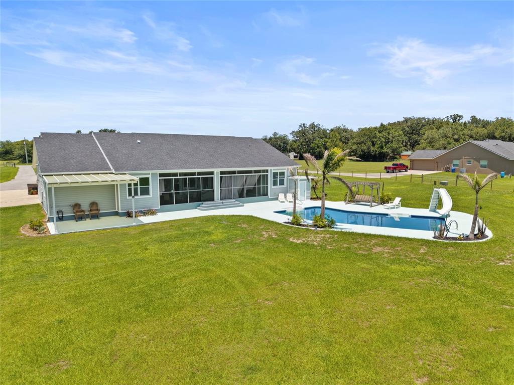 An aerial view of a house exterior featuring a covered patio, pool, and large lawn — 15710 COLDING LOOP, WIMAUMA, FL