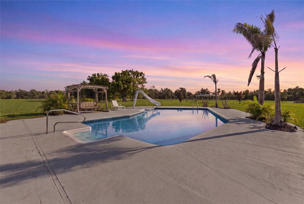 A swimming pool with a slide and a wooden swing set on a grassy lawn — 15710 COLDING LOOP, WIMAUMA, FL
