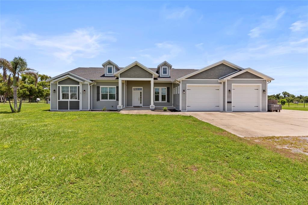 A gray, single-story house with a two-car garage and two dormer windows sits on grass — 15710 COLDING LOOP, WIMAUMA, FL