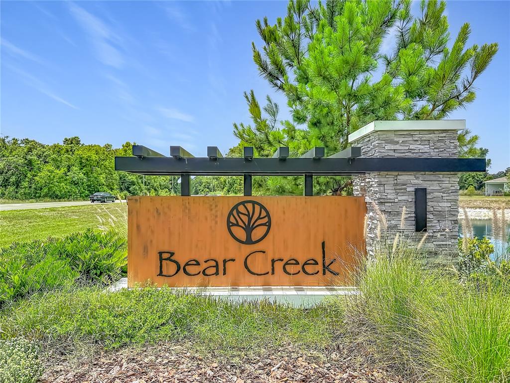 A metal sign with the words Bear Creek stands in front of a stone pillar — 11994 GRIZZLY LANE, NEW PORT RICHEY, FL
