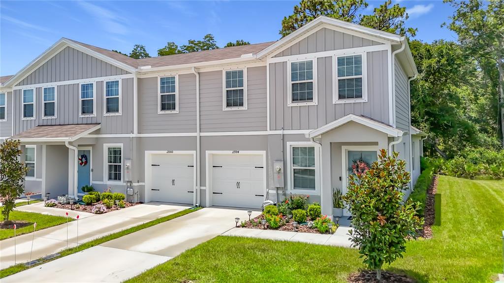 A two-story townhouse exterior features gray siding, white trim, two garage doors, and landscaped lawns — 11994 GRIZZLY LANE, NEW PORT RICHEY, FL