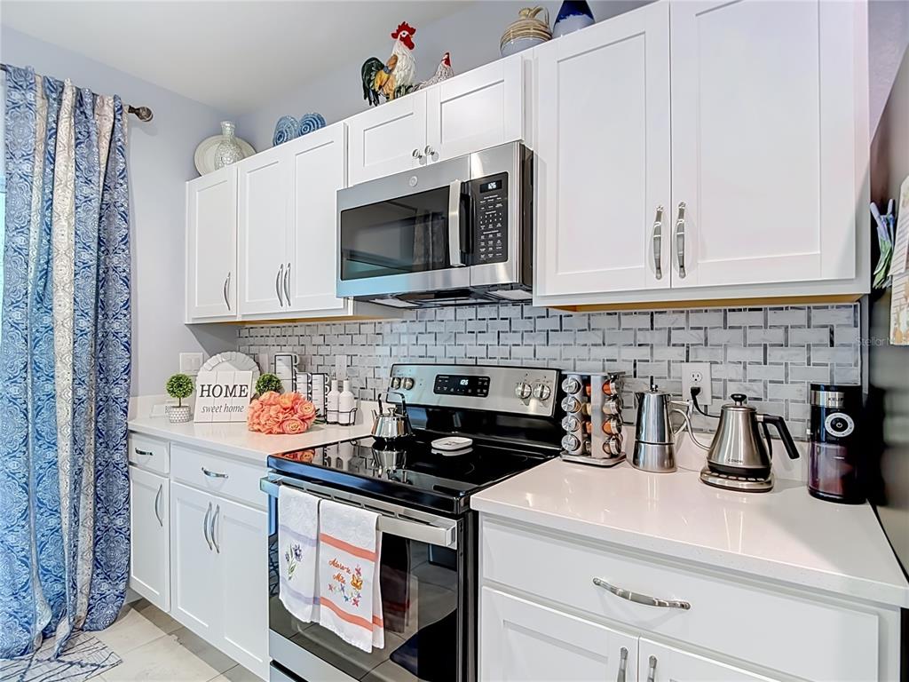 A kitchen features white cabinets, a stainless steel microwave, a black stove, and tiled backsplash — 11994 GRIZZLY LANE, NEW PORT RICHEY, FL