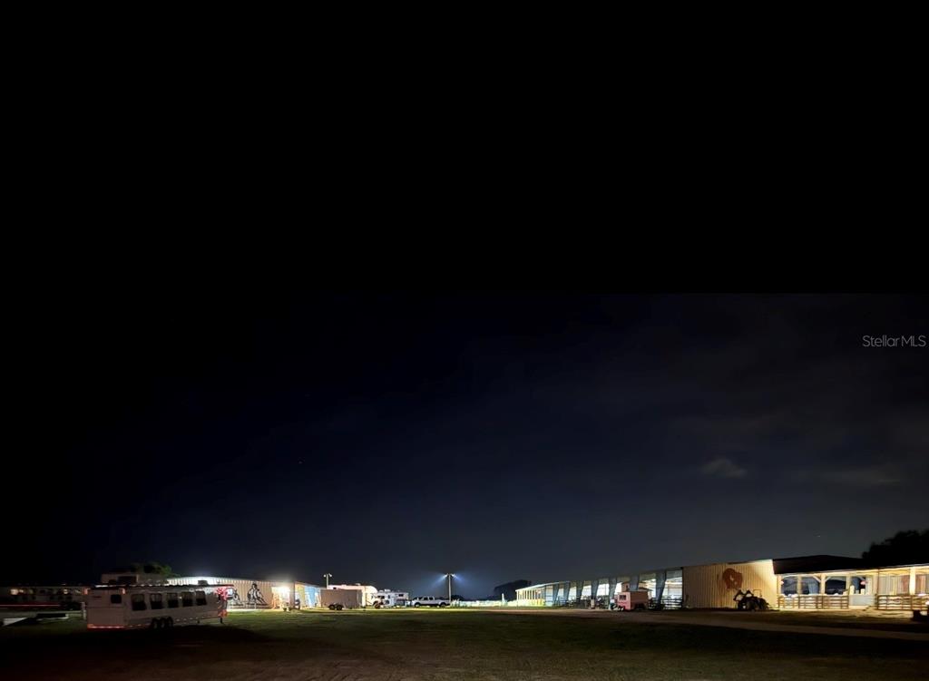 An exterior view of a barn and outbuildings at night with illuminated parking areas — 40812 GRAYS AIRPORT ROAD, LADY LAKE, FL