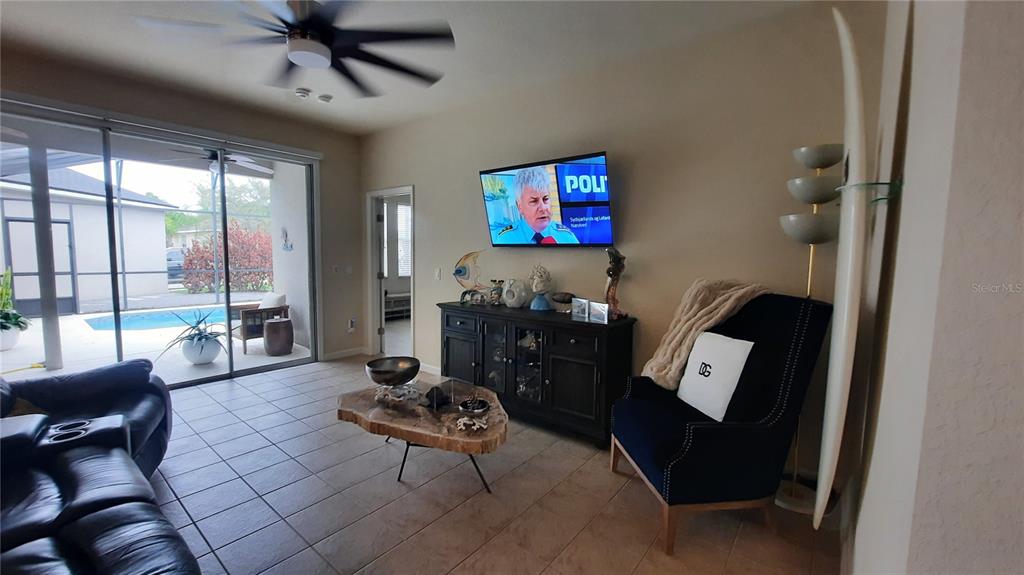 A living room features tile flooring, a dark media console, a surfboard, and pool access — 4959 THAMES STREET E, KISSIMMEE, FL
