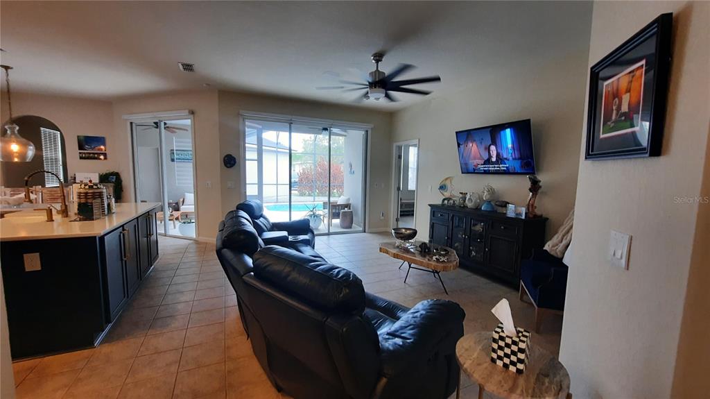 A living room with a dark leather sofa, television, and sliding glass doors to a pool — 4959 THAMES STREET E, KISSIMMEE, FL