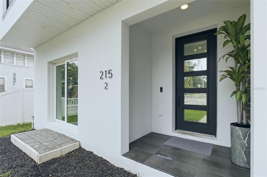A modern home entrance features a black glass-paneled door, white stucco walls, and tiled porch — 215 W COLUMBUS DRIVE UNIT 2, TAMPA, FL