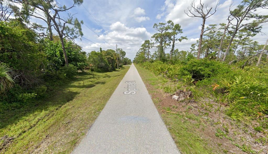 A paved road stretches through a rural area surrounded by dense trees and vegetation — 4481 SPIRE STREET, PORT CHARLOTTE, FL