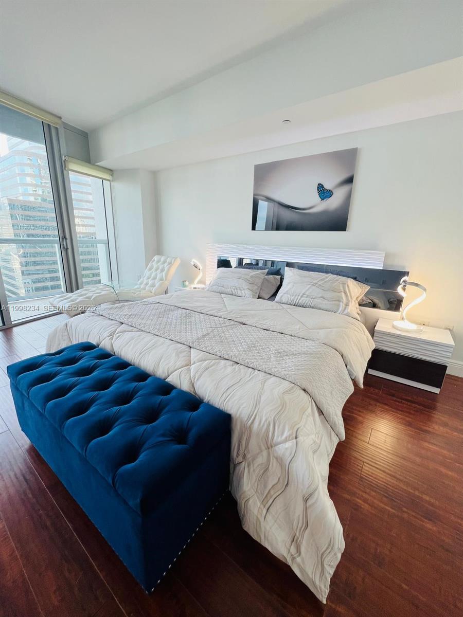 A bedroom features a blue tufted bench, a white bed, and floor-to-ceiling windows — 495 Brickell ave # 2707, Miami FL 33131, MIAMI, FL
